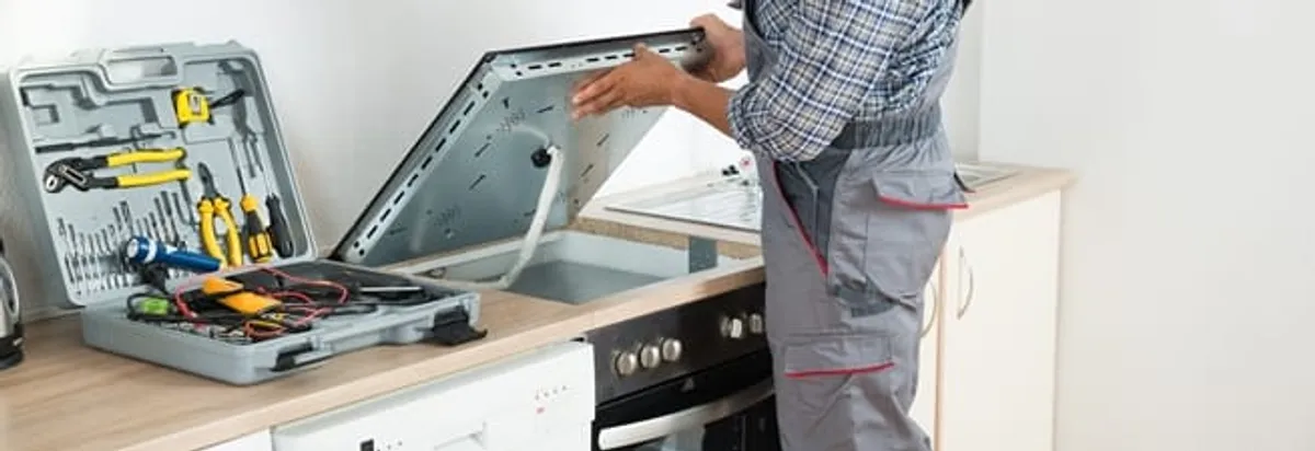 Cooktop repair technician lifting a built-in stovetop for service in Duluth, MN